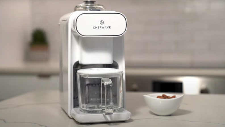 A ChefWave Milkmade vegan milk maker in the kitchen. Next to it, there's a bowl of almonds.