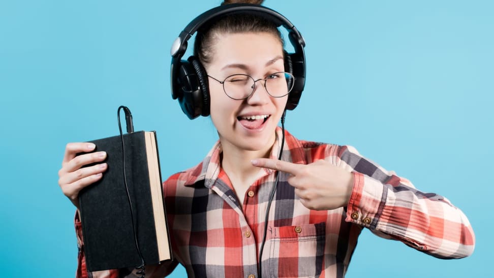 A person wearing headphones points to a book signifying they're listening to an audiobook.