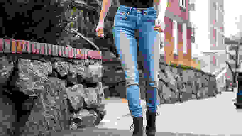 A woman walking down the street in a black shirt and Good American skinny jeans