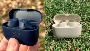 On left, black Jabra Elite 4 Active Wireless Earbuds held in a hand before a leaf-covered ground. On right, next to cream Jabra Elite 5 Earbuds outdoors on grass.