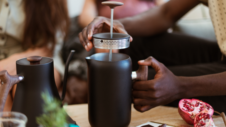 A person is lifting the lid from a Fellow Clara French press in a living room.