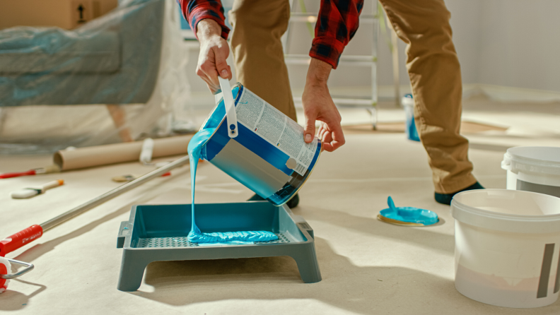 Person pouring teal paint into a paint tray