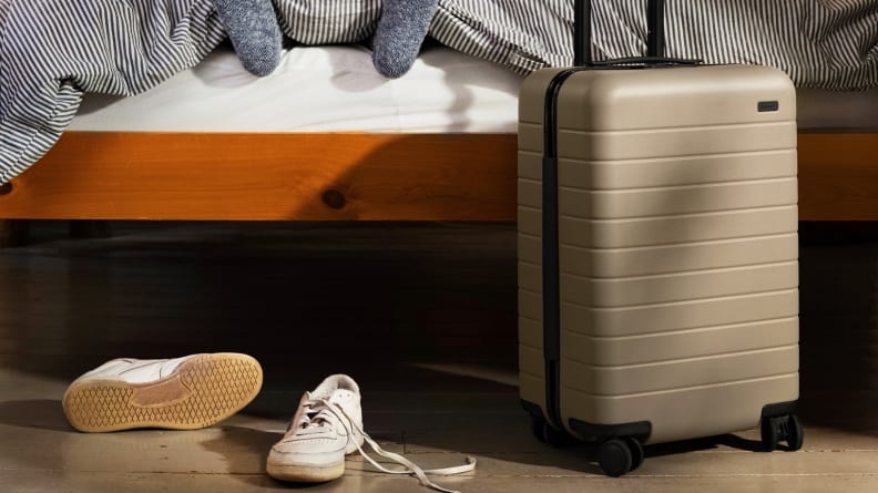 Silver-toned hard shell suitcase next to bed and white sneakers