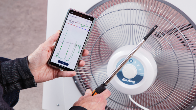 A close-up of someone holding a smart anemometer up to a fan.