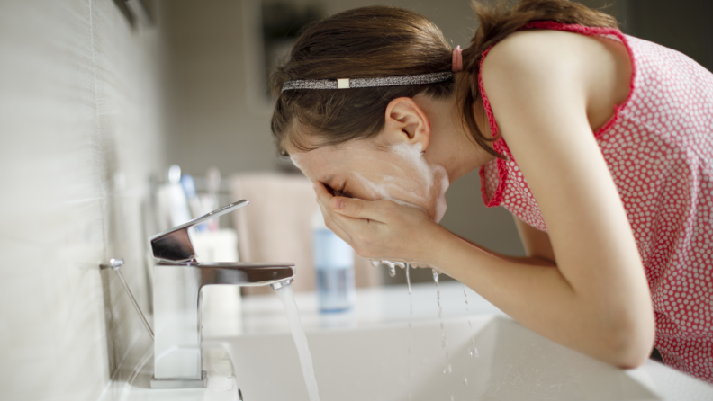 Person washing their face in a bathroom sink