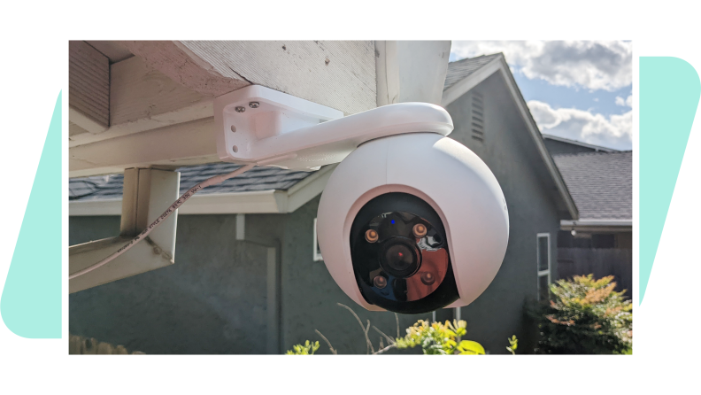 The EzViz H8 Pro 3K outdoor camera mounted to a house outside, with a green background.