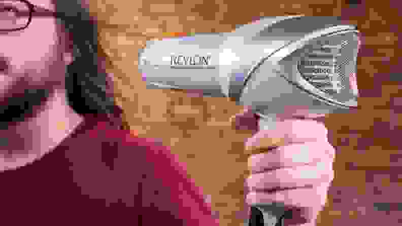 A person with long hair holding a silver hair dryer up to dry their hair.