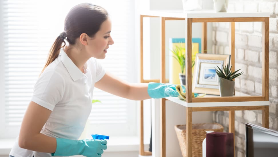 Woman wearing blue rubber gloves and spray bottle to wipe off surface in home.