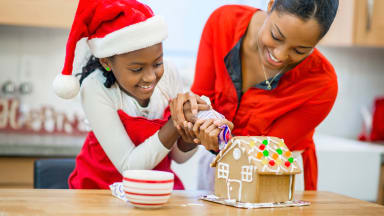Adult and child wearing red in Santa hat decorating a gingerbread house