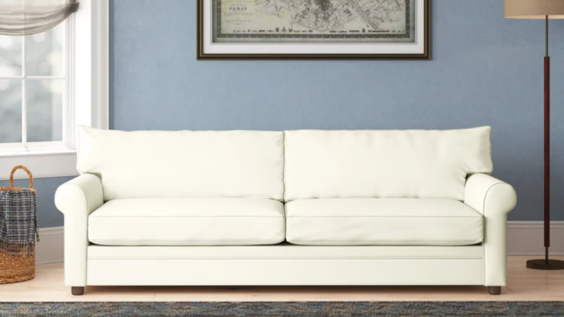 An armless white sofa placed in the living room in front of a round coffee table.