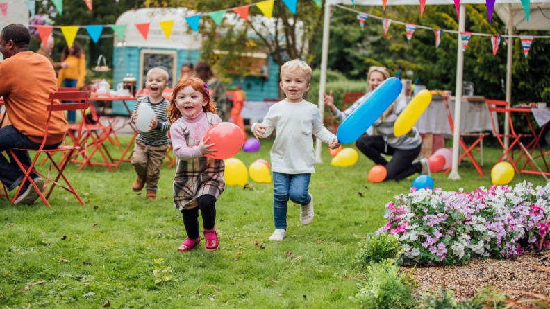 Children running through the garden with balloons during a party.