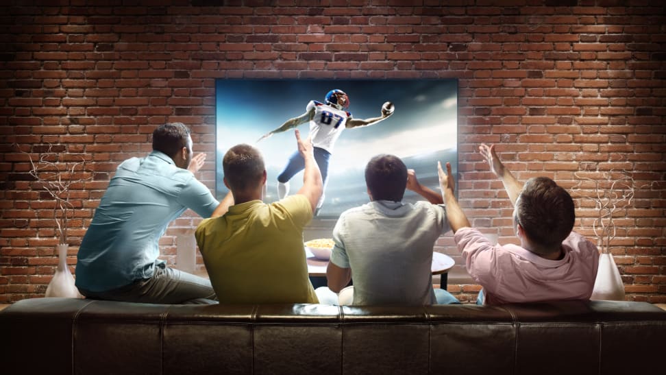 Four guys cheering in multi-colored shirts while watching football on a big-screen TV