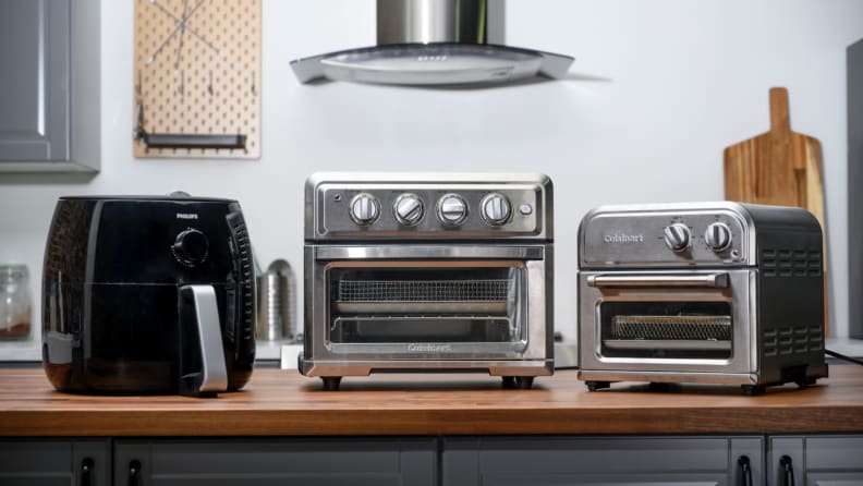 Three different air fryers sit on a wood counter.