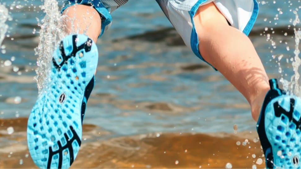 A child jumps in water with turquoise-colored water shoes