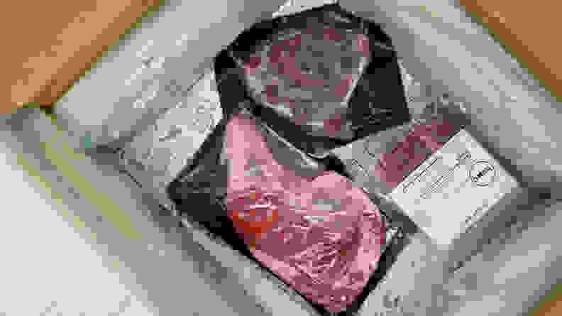 Open Crowd Cow package shot from above, with packing materials and three pieces of raw packaged meat visible.