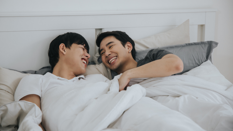Two men laughing in bed