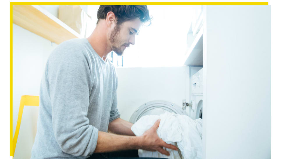 A person taking white sheets out of a drying machine.