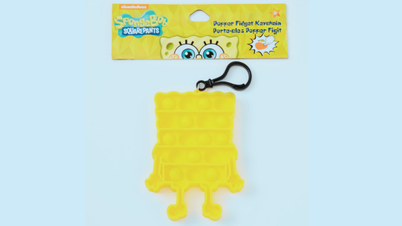 A yellow pop-it in a plastic bag is shaped like cartoon character SpongeBob SquarePants and has a black keychain on top