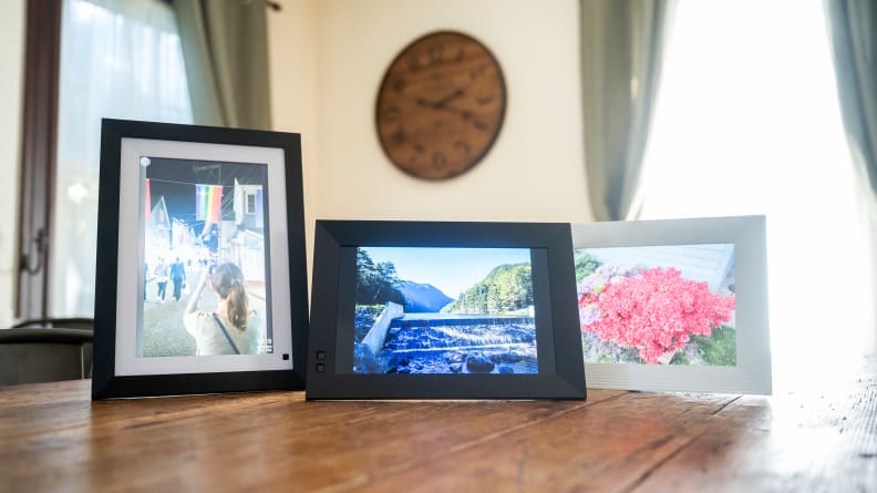 Three digital picture frames displaying colorful florals sit on a wooden table.