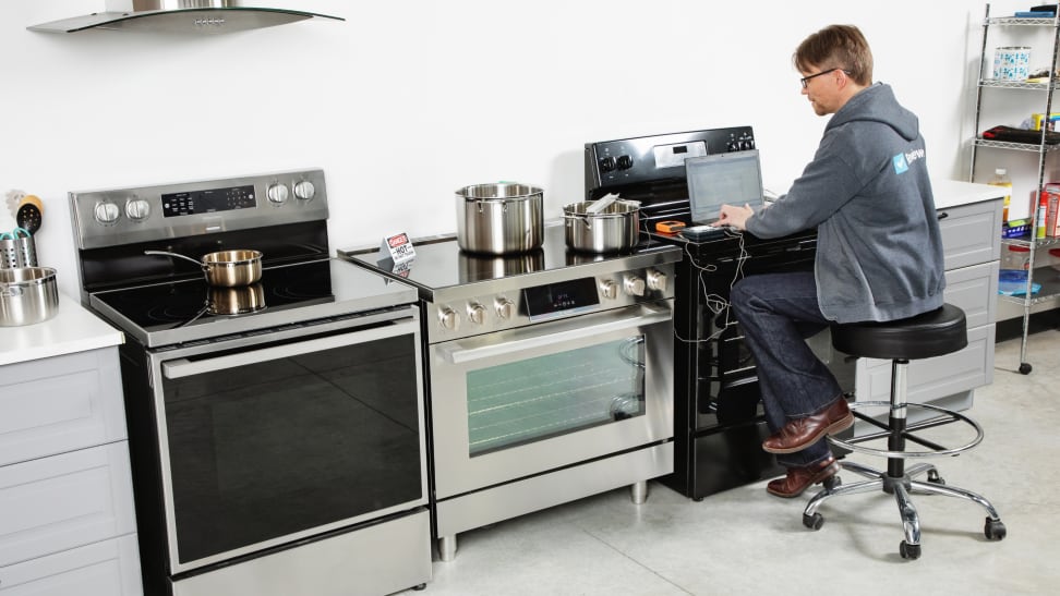 A Reviewed Kitchen editor sitting at one of three stoves, typing on a laptop.