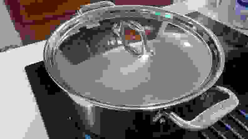 Large stainless pot with lid attached on stovetop.