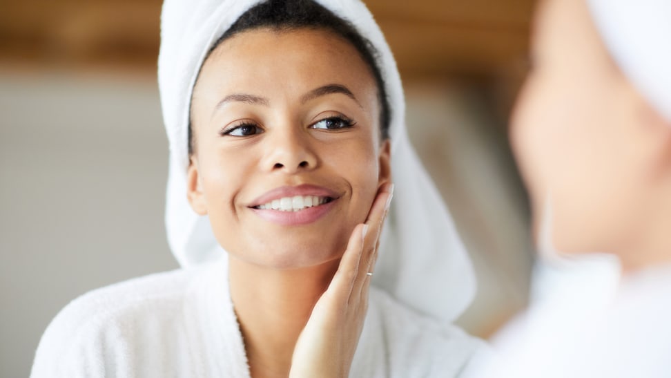 Woman looking into a mirror and smiling as she touched her cheek.