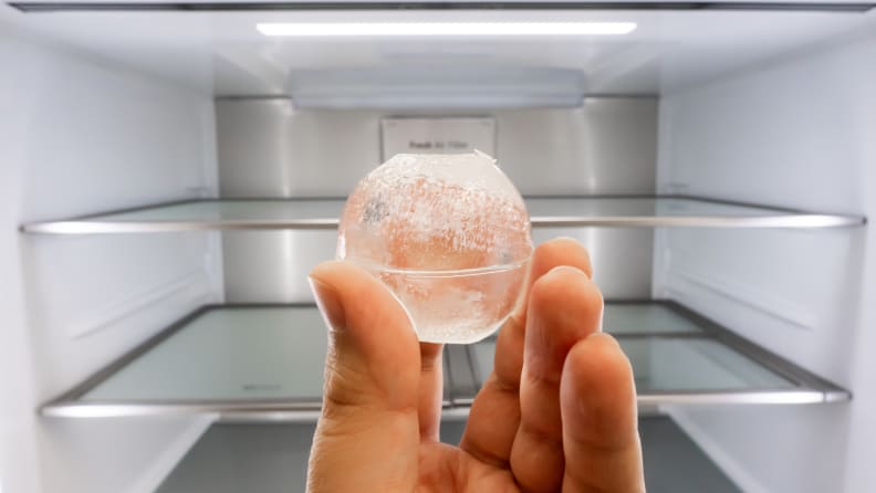 A close-up of a hand holding up a spherical ice cube.