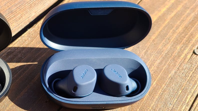 A pair of blue earbuds sits on a wooden plank with their case open.