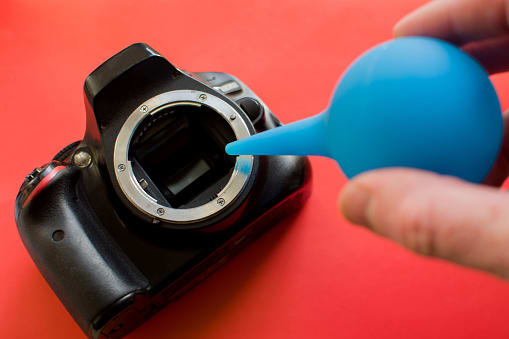 Photographer cleaning photocamera light sensor. Cleaning matrix SLR camera with air. Rocket Air Blower blows off dust particles. Small roughness sharpness