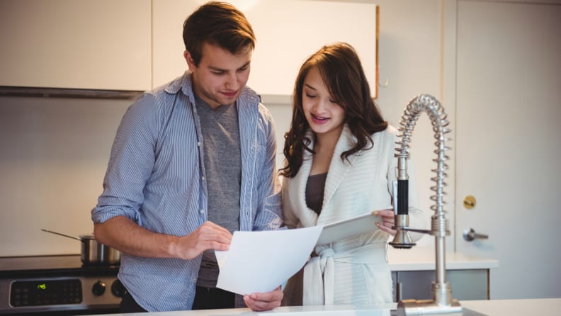 A couple stands in a kitchen reviewing paperwork together near the sink and stove.