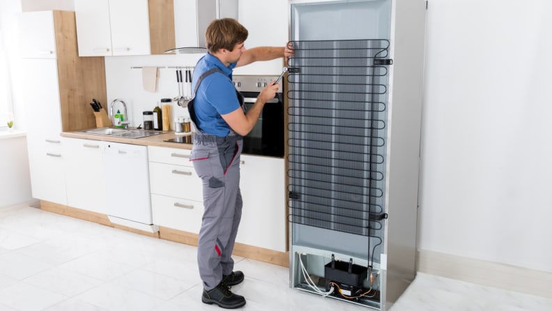 A repair person working on the back of a refrigerator