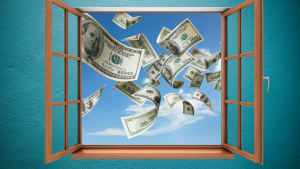 Dollar bills fly out an open window into a blue sky