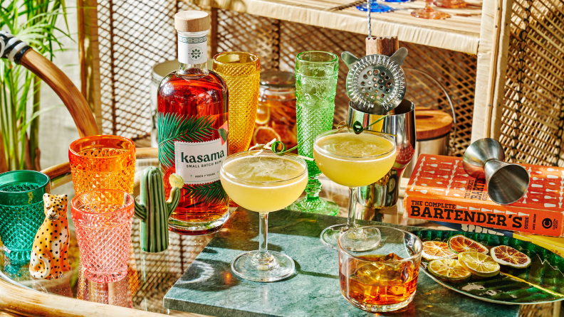On a cocktail table, a bottle of Kasama aged rum is the main focus. Around the bottle there are a few glasses of cocktails.
