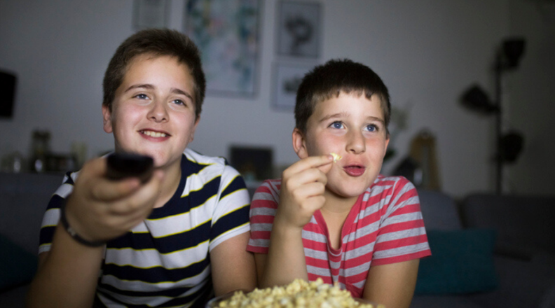 Two boys sit on the couch and watch TV