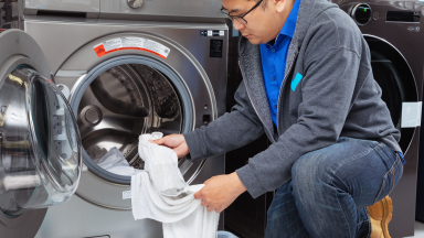 An Asian man pulls white socks and towels out of a washing machine