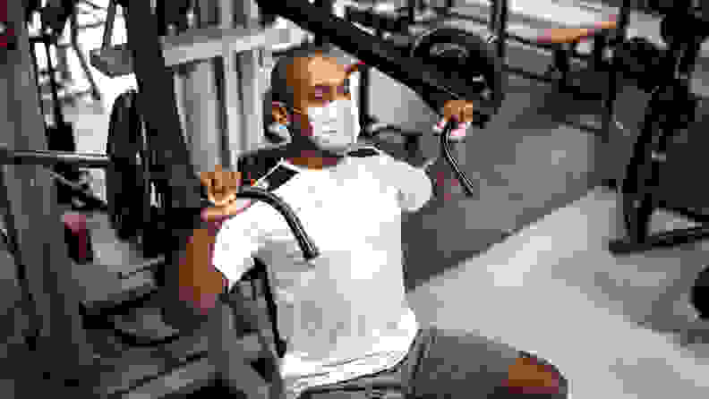 Man doing strength workout exercise in gym with face mask.