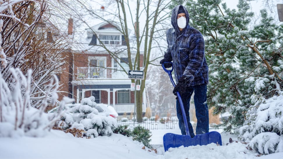 Man shoveling snow while wearing protective face mask.