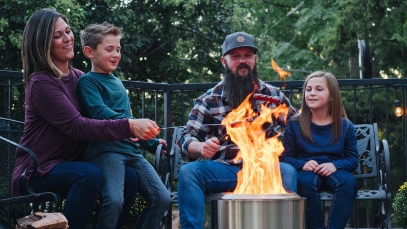 Four people gather around a portable fire pit.