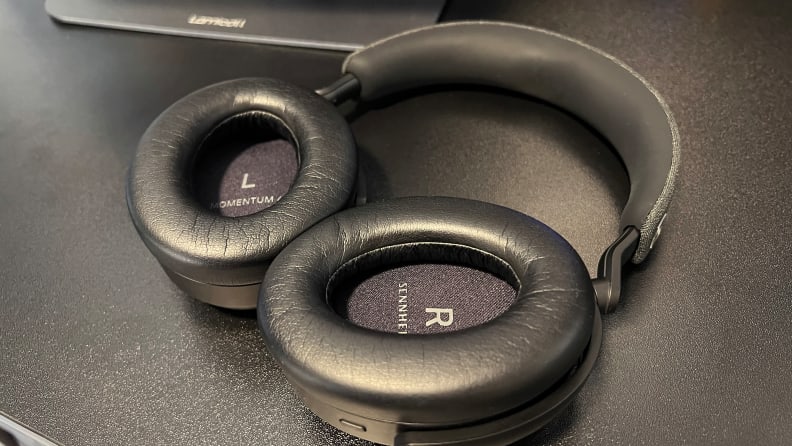 A pair of black headphones sits on a black desk with leatherette earpads showing.