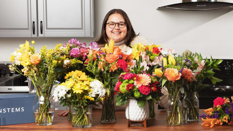 A person standing behind a variety of flower arrangements.
