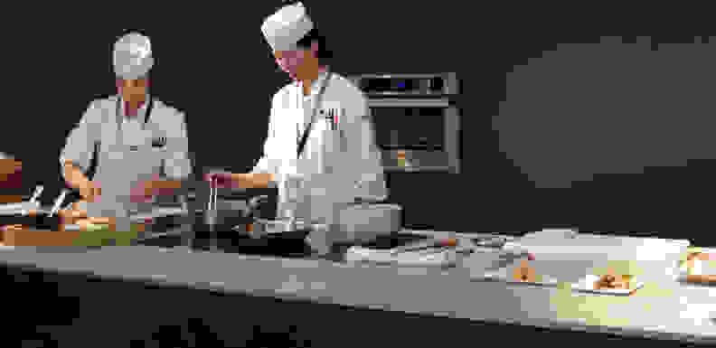 Chefs prepare traditional Japanese food using a Panasonic wall oven and induction cooktop.