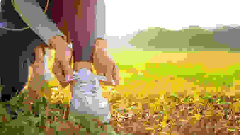 A woman tying her sneakers in grass.