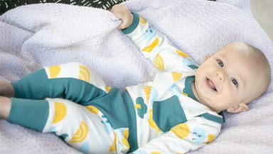 Baby smiling on blanket while wearing green and yellow clothing set.
