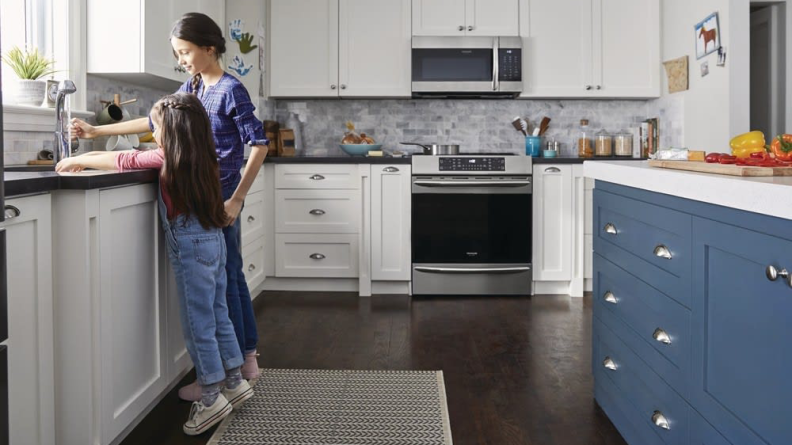 A parent and child wash dishes in a kitchen.