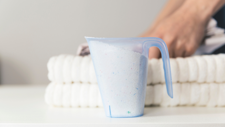 Person folding white towels next to cup of powdered detergent.