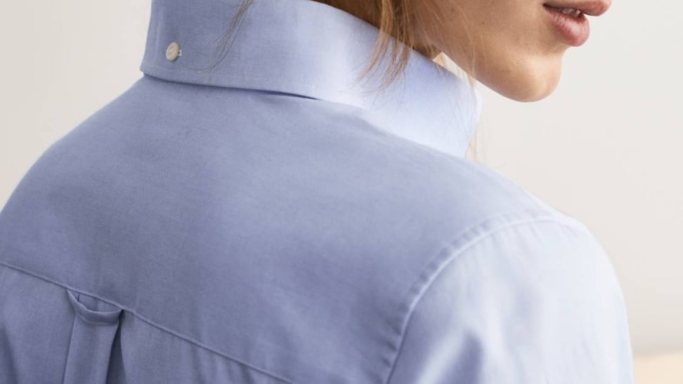 Woman wearing blue oxford button-down shirt with locker loop visible.