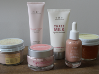 FarmHouse Fresh Mighty Tighty Turmeric & Banana Tightening Mask, Whoopie! Shea Butter Hand Cream, Full Moon Dip, Three Milk Ageless Moisturizer, Pink Dust Illuminating Peptide Serum and Honey Lavender Salt Body Scrub all gathered together on top of wooden surface.