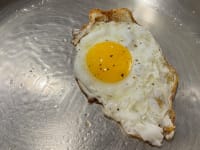 An egg cooked on a stainless-steel pan.