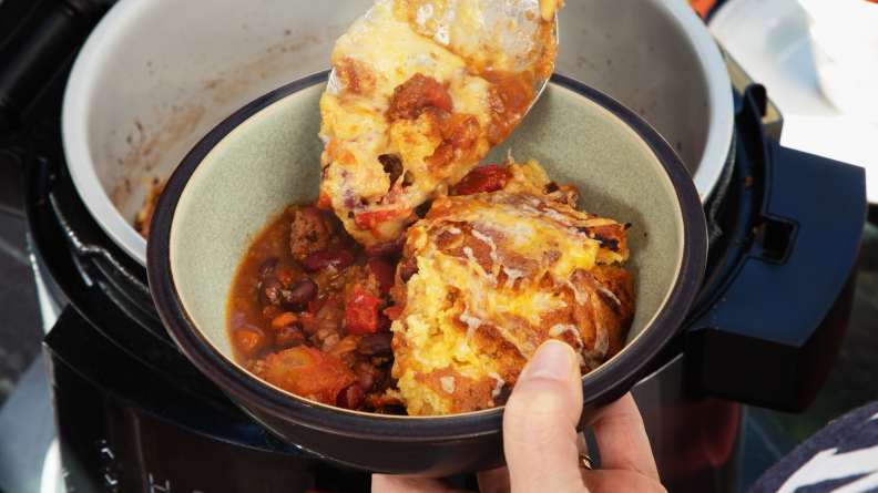 Hand holding a bowl full of cornbread-topped chili