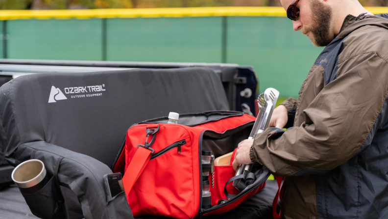 Red camping cooler with a man pulling water out of it